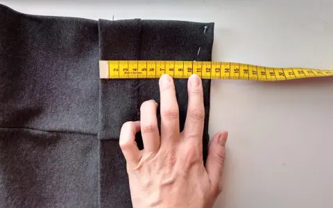 Mierzysz, jak skrócić spodnie ręcznie. Miarka krawiecka pokazuje ok. 11 cm.