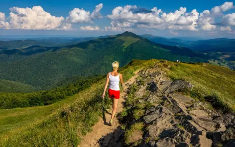 Kobieta wędruje szlakiem pośród zielonych wzgórz. Bieszczady jakie to góry – rozległe, malownicze, z dalekimi horyzontami.