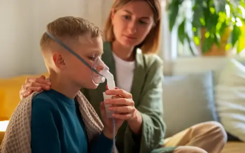 Chłopiec z maską nebulizatora, wspierany przez matkę. Dbałość o zdrowie dziecka z astmą wczesnodziecięcą.