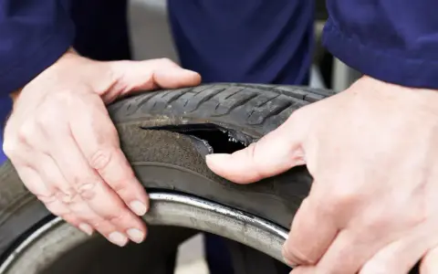 Dłonie mechanika badają oponę po głośnym wystrzale. Widoczne jest duże rozdarcie bieżnika.