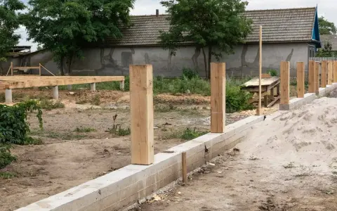 Budowa fundamentu pod ogrodzenie: betonowy murek, drewniane słupki i piasek.
