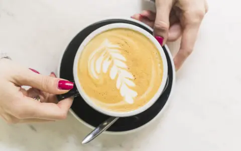 Une main tient une tasse de café latte avec un dessin de feuille. Un guide pour comment faire un latte parfait.