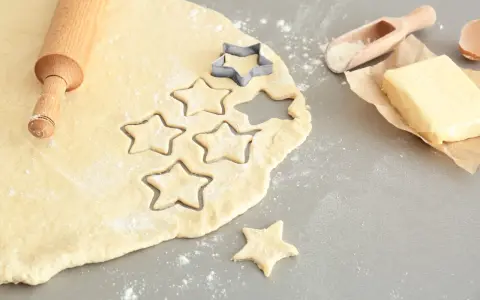 Plätzchenteig zu krümelig? Sterne werden ausgestochen. Teig, Nudelholz, Butter und Mehl sind bereit für leckere Kekse.