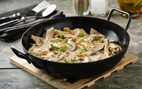 Herzhaftes geschnetzeltes mit Pilzen in cremiger Sauce, garniert mit Petersilie, serviert in einer schwarzen Pfanne.