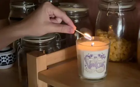 Encendiendo una vela decorada, parte de manualidades para decorar velas, con frascos de vidrio de fondo.