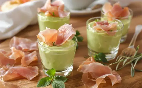 Petits verrines de mousse de chevre onctueuse, garnies de fines tranches de jambon cru et de quelques herbes fraîches.