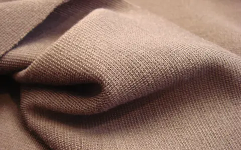Braune Stofffalten, die die glatte, feine Struktur von Single Jersey zeigen. Dieses Material ist weich und dehnbar.