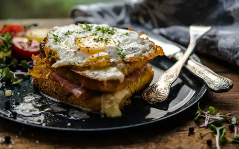 Un croque-madame gourmand, un des plats typiques parisiens, avec un œuf au plat, jambon et fromage fondant, servi avec des tomates et des pousses.