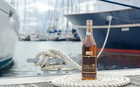 Butelka Bas Armagnac Chateau de Laubade stoi na tle jachtów. To doskonały trunek, jeśli zastanawiasz się, armaniak co to.