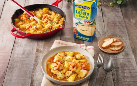 Un delicioso rape a la marinera, con patatas y gambas, servido en una cazuela roja y un plato.