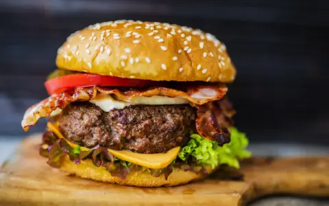 Hamburger di carne succulento con bacon croccante, formaggio fuso, pomodoro e lattuga su panino ai semi di sesamo.