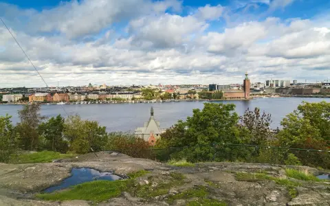 Vy över Riddarfjärden från Skinnarviksberget Stockholm, med Stadshuset i bakgrunden under en molnig himmel.