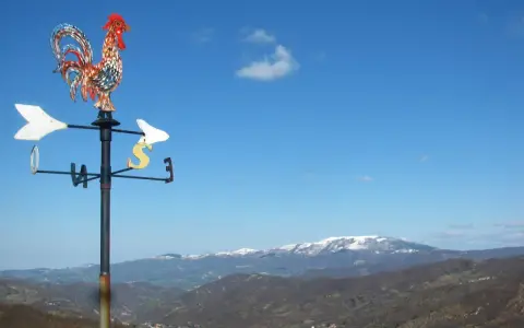 Gallo segnavento su sfondo azzurro, con montagne innevate all'orizzonte. Un invito a scoprire cosa vedere in Valmarecchia.