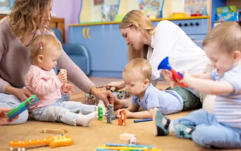 Opiekunki bawią się z dziećmi zabawkami na dywanie w żłobku.