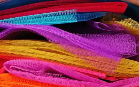 Un tas de **tulle** aux couleurs vives : orange, rose, jaune, violet, bleu et rouge.