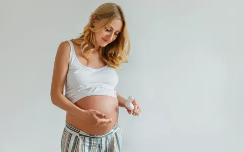 Ciężarna kobieta delikatnie wmasowuje krem z kwasem hialuronowym w brzuszek, dbając o skórę w tym wyjątkowym czasie.