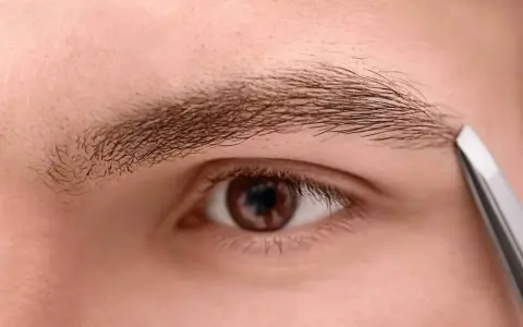 Un homme utilise une pince à épiler pour tailler un sourcil qui rebique, affinant son regard.