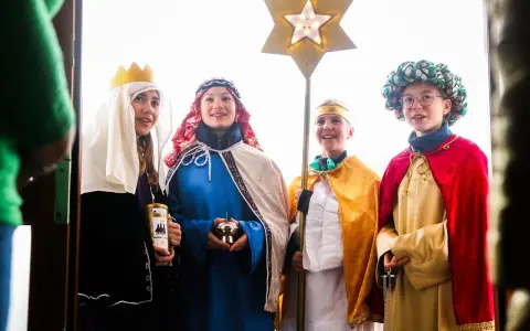 Vier Kinder als Sternsinger evangelisch verkleidet, mit Stern und Spendenbüchse, stehen vor einer Tür.