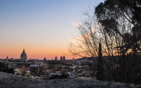 Un magico pincio roma tramonto con cupole che si stagliano contro il cielo aranciato, alberi spogli in primo piano.