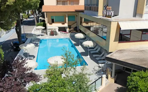 Piscina invitante e lettini prendisole al **hotel Simon Gatteo Mare**. Ombrelloni bianchi e vegetazione rigogliosa creano un'oasi di relax.