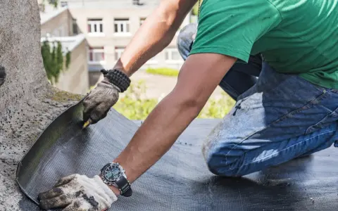 Trabajador realiza impermeabilización de terrazas, cortando material para asegurar la protección contra el agua.