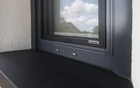 Szary parapet zewnętrzny pod oknem z moskitierą. Zastanawiasz się, czym przykleić parapet zewnętrzny blaszany?