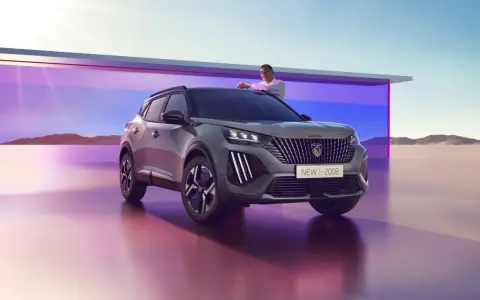 Mężczyzna opiera się o maskę nowego Peugeot E-2008, stylowego peugeot suv, na tle futurystycznej architektury i pustynnego krajobrazu.