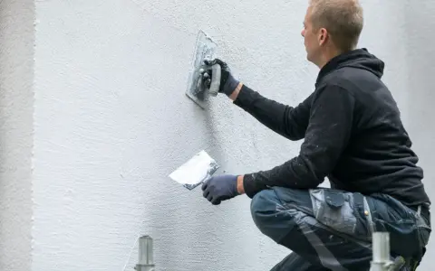 Artisan appliquant un enduit gratté sur un mur extérieur.