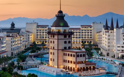 Luksusowy hotel z basenami i wieżą, idealny na wakacje all inclusive w Turcji. Góry w tle.