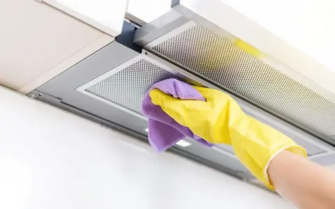 Mano con guante amarillo y paño morado limpiando la campana extractora por dentro.