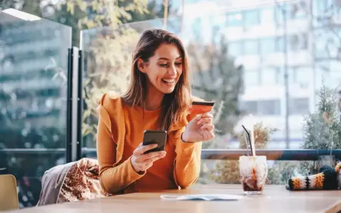Smiling woman uses phone and credit card. She's researching if you need an LLC for a business credit card.