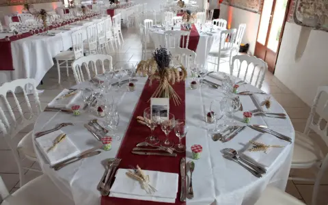 Une table dressée à la française, prête pour un événement. Nappes blanches, chemins de table bordeaux, vaisselle et couverts élégants, et une touche champêtre avec des épis de blé et de la lavande.