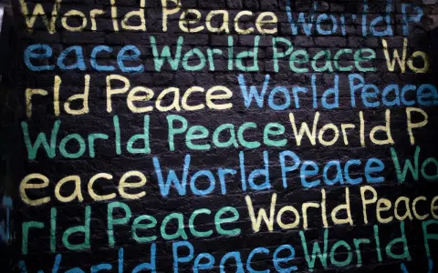 Un promemoria di Gianni Rodari: "Pace nel mondo" scritto in giallo, blu e verde su un muro di mattoni neri.