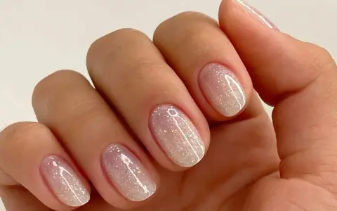 Nahaufnahme einer Hand mit ovalen Nägeln, die mit schimmerndem Glitzer-Nagellack in Pastelltönen verziert sind.