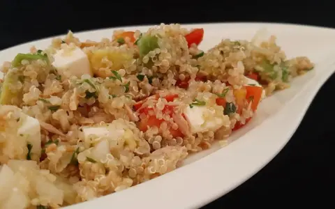 Salade colorée de quinoa avec des dés de feta, avocat, tomates et persil, servie dans un plat blanc.