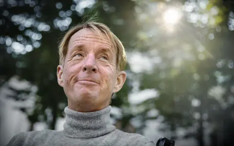 En leende man med rullstol, kanske en scen från filmer med Nils Hallberg, tittar upp mot solen.