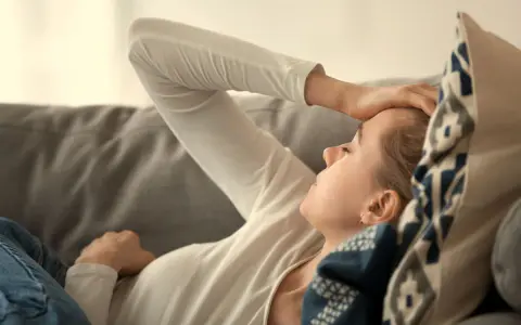 En kvinna med handen mot pannan, utmattad. Kan vara tecken på b12-brist stress.