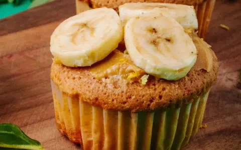 Pyszne muffinki bananowe fit z masłem orzechowym i plasterkami banana na drewnianej desce.
