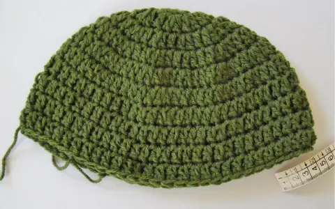 Gorro de lana verde tejido a mano, ideal para aprender como tejer un gorro de lana para principiantes. Cinta métrica al lado.
