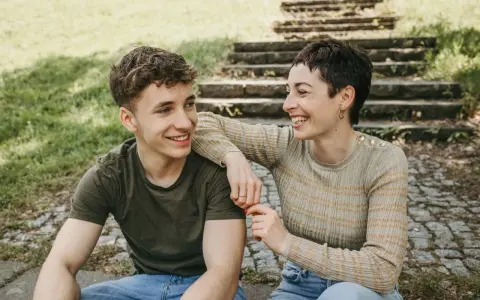 Ein lachendes Mutter-Sohn-Gespann sitzt im Freien vor einer Steintreppe.