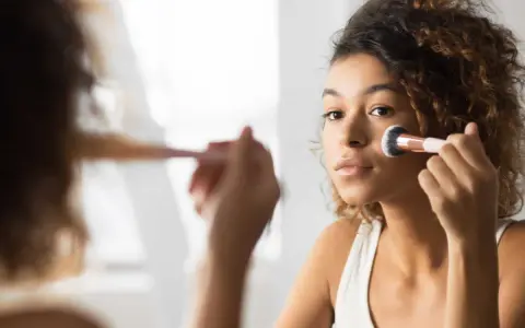 Une jeune femme applique du fond de teint avec un pinceau. Elle se demande combien de temps garder une palette de maquillage pour une peau parfaite.