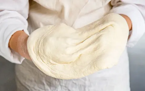 Hände halten geschmeidigen pizzateig, original rezept von einem italienischen gastronomen. Perfekt für authentische Pizza.