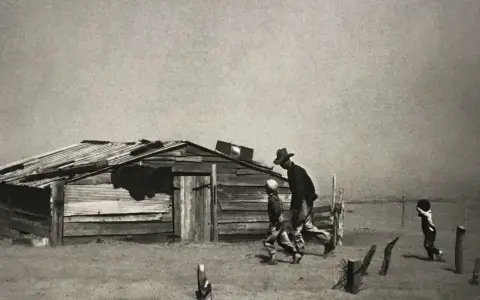 Dust Bowl migrants walk past a dilapidated shack in this iconic Arthur Rothstein photo, a stark reminder of hardship.