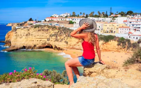 Kobieta w kapeluszu podziwia malownicze portugalia wybrzeże algarve z białymi domkami i turkusową wodą.