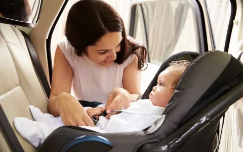 Madre abrochando el cinturón de seguridad a su bebé en la silla del coche. Los niños en el coche viajan seguros.