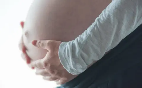 Dłonie obejmujące ciążowy brzuch, odczuwając ucisk na pęcherz w ciąży w II trymestrze.