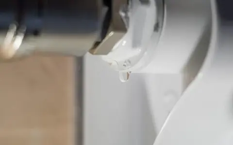 Una gota de agua cae de la rosca de un radiador. El radiador pierde agua por la rosca, indicando una posible fuga.