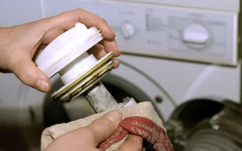 Hände reinigen das Flusensieb einer Bosch Waschmaschine. Regelmäßige Pflege sorgt für einwandfreie Funktion.
