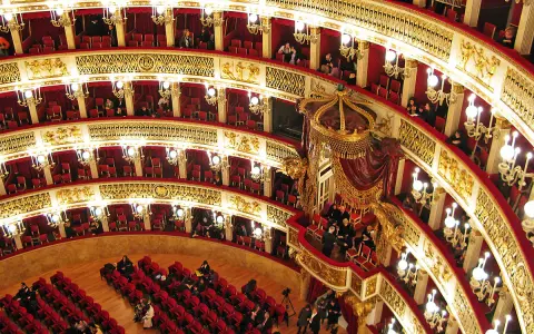 Elegancka loża w teatrze, z czerwonymi aksamitnymi siedzeniami i złotymi zdobieniami, czeka na widzów.