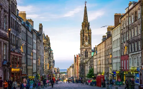 Edinburgh's Royal Mile with a clock tower and people walking on a cobblestone street.
